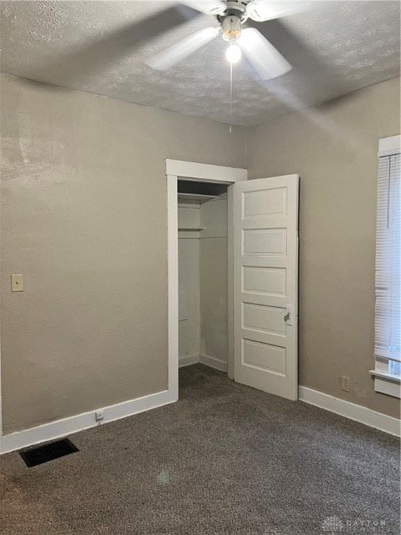 unfurnished bedroom with ceiling fan, a closet, a textured ceiling, and dark colored carpet