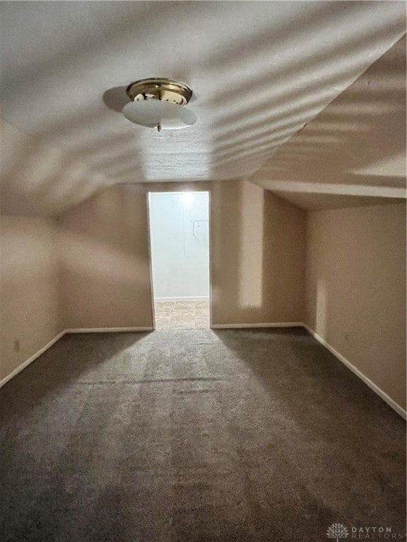 bonus room with dark carpet and vaulted ceiling