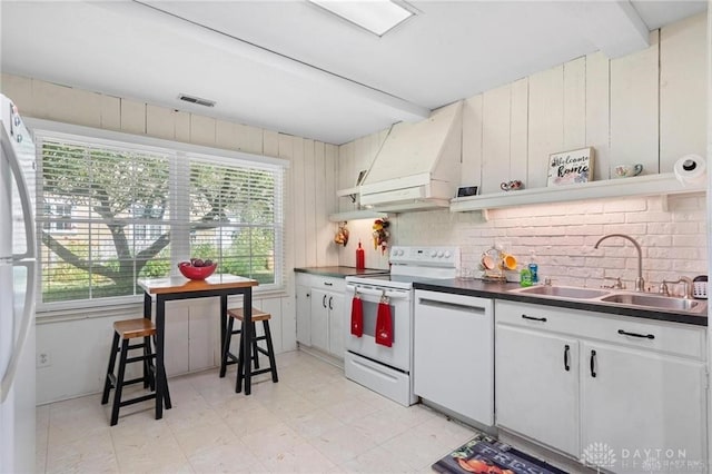 kitchen with a wealth of natural light, custom exhaust hood, white appliances, sink, and white cabinetry