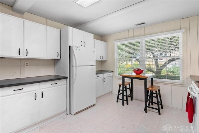 kitchen with white fridge, white cabinetry, and wooden walls