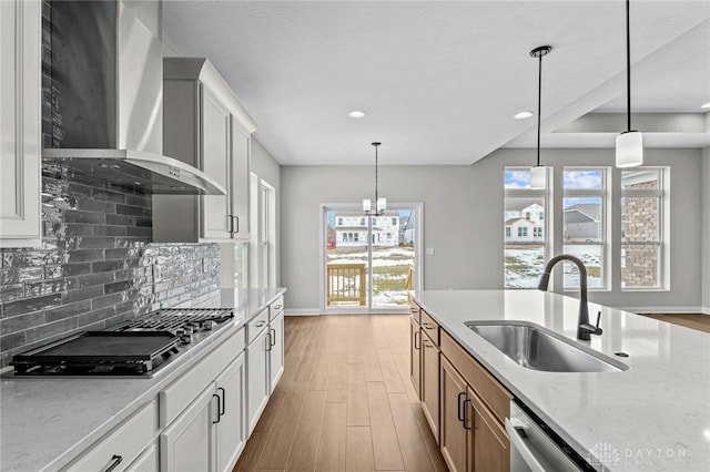 kitchen featuring pendant lighting, white cabinets, a sink, wall chimney range hood, and light stone countertops