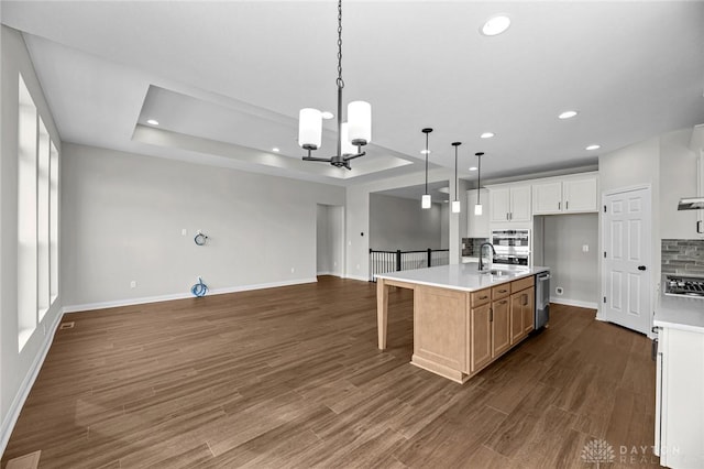 kitchen with a kitchen island with sink, white cabinets, open floor plan, light countertops, and decorative light fixtures