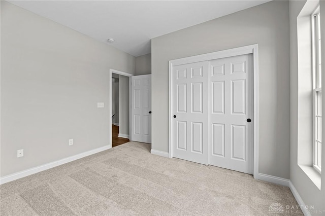 unfurnished bedroom featuring baseboards, a closet, and light colored carpet