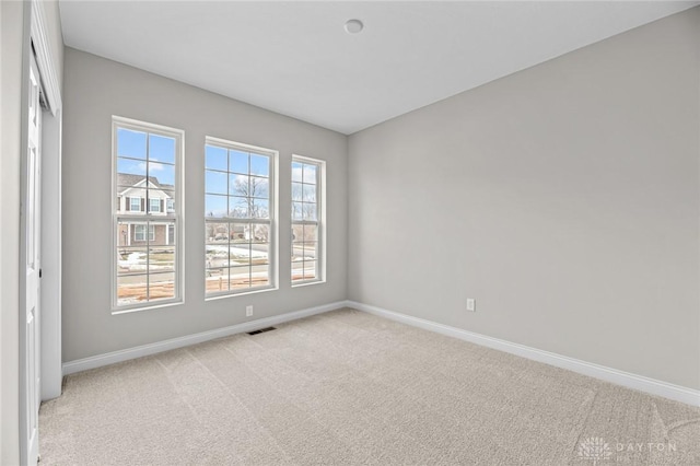 empty room featuring light carpet, visible vents, and baseboards