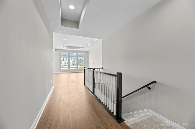 hall featuring baseboards, a raised ceiling, wood finished floors, and an upstairs landing