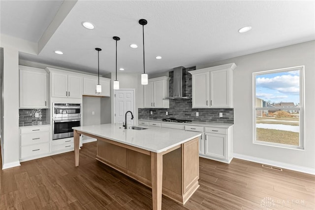 kitchen with wall chimney exhaust hood, an island with sink, gas cooktop, and white cabinets