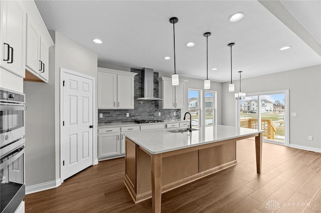 kitchen featuring light countertops, white cabinets, a kitchen island with sink, and wall chimney exhaust hood