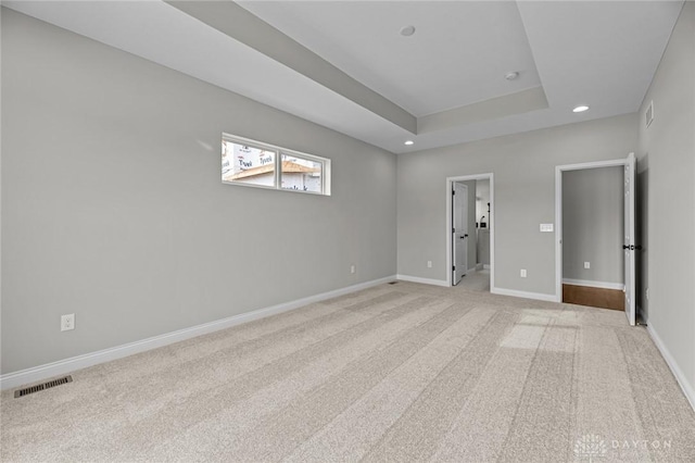 spare room with recessed lighting, a raised ceiling, visible vents, light carpet, and baseboards