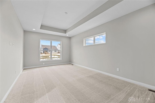 spare room featuring light carpet, a raised ceiling, and baseboards