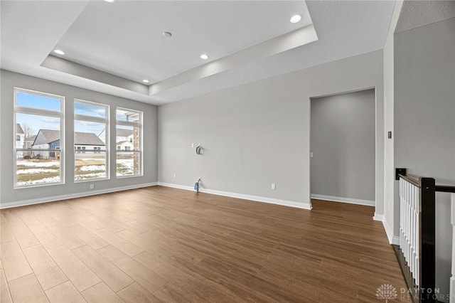 unfurnished room with wood finished floors, recessed lighting, a raised ceiling, and baseboards