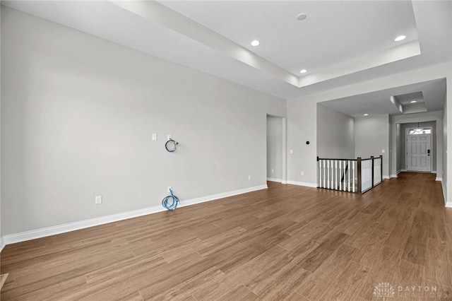 empty room with baseboards, a tray ceiling, wood finished floors, and recessed lighting