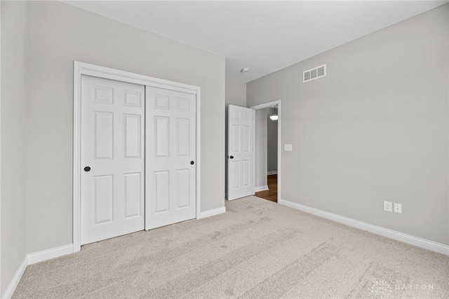 unfurnished bedroom with baseboards, visible vents, a closet, and light colored carpet