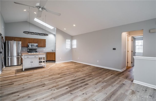 kitchen featuring a skylight, stainless steel appliances, light countertops, light wood-style flooring, and brown cabinetry