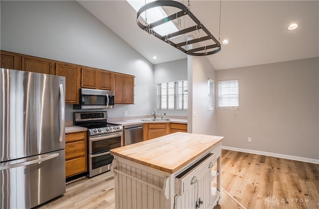 kitchen with appliances with stainless steel finishes, a sink, wood counters, light wood-type flooring, and baseboards