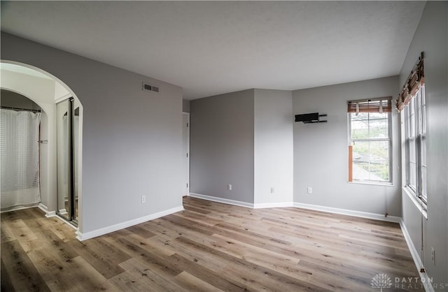 empty room featuring arched walkways, visible vents, baseboards, and wood finished floors