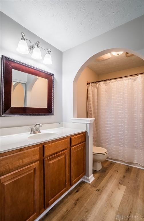 full bathroom featuring a shower with shower curtain, toilet, wood finished floors, a textured ceiling, and vanity