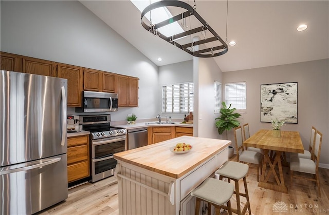 kitchen featuring appliances with stainless steel finishes, a kitchen breakfast bar, light wood-type flooring, wooden counters, and a sink