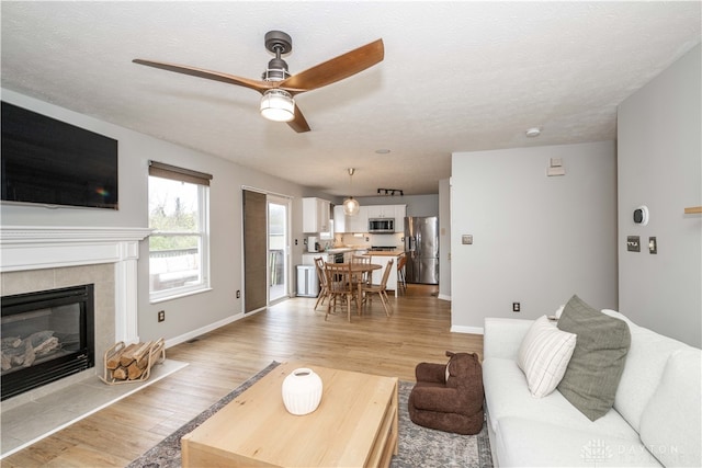 living room featuring ceiling fan, light wood-type flooring, a textured ceiling, and a tile fireplace