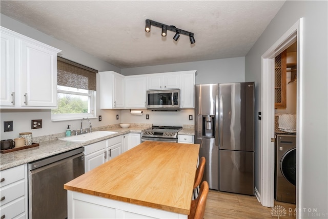 kitchen with appliances with stainless steel finishes, sink, light hardwood / wood-style flooring, white cabinets, and washer / dryer