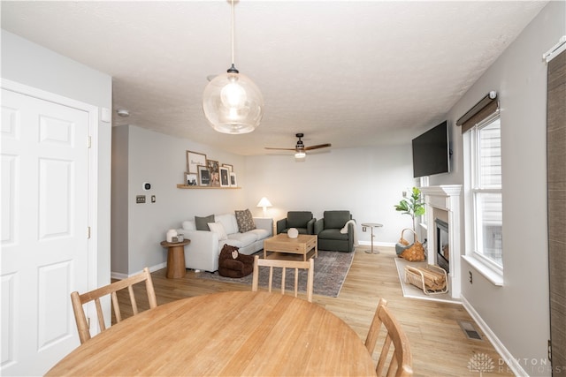 dining area with a textured ceiling, light wood-type flooring, and ceiling fan