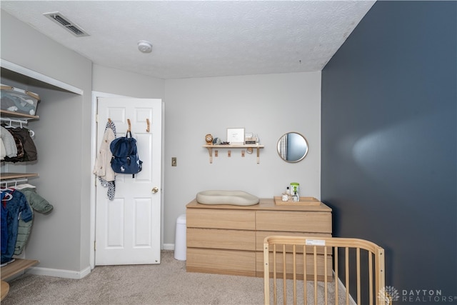 bedroom featuring light carpet, a textured ceiling, and a crib