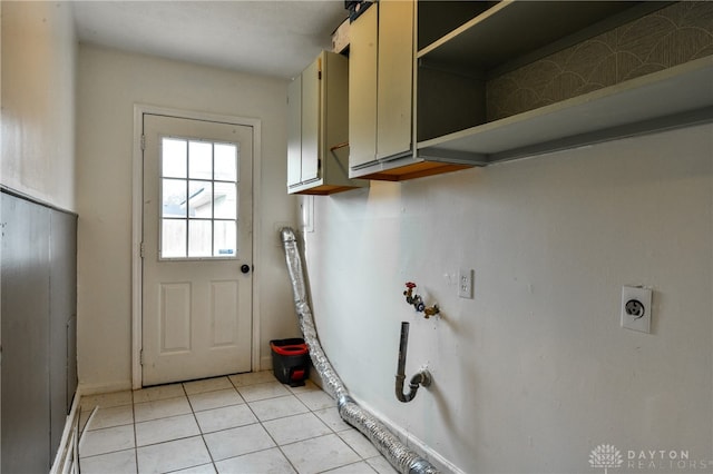 laundry room featuring electric dryer hookup, light tile patterned flooring, and cabinets