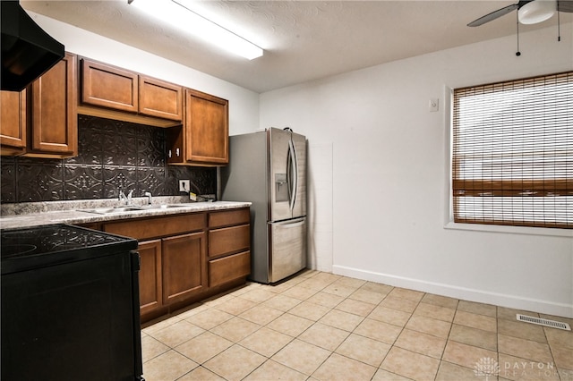 kitchen featuring black range oven, ventilation hood, sink, decorative backsplash, and stainless steel fridge