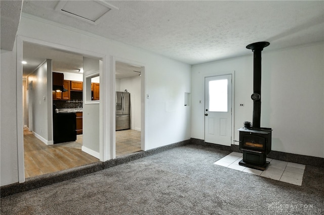 unfurnished living room featuring a wood stove, light colored carpet, and a textured ceiling