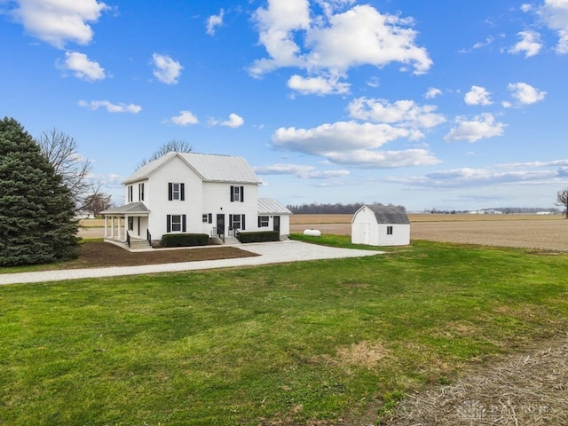 rear view of property featuring a storage unit, a rural view, and a yard