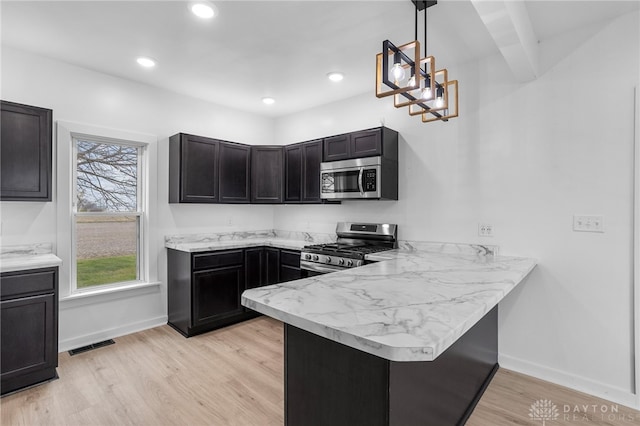 kitchen featuring kitchen peninsula, appliances with stainless steel finishes, beam ceiling, decorative light fixtures, and light hardwood / wood-style floors