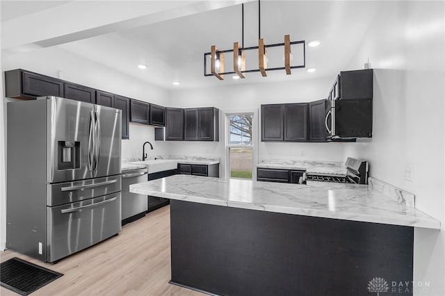 kitchen with stainless steel appliances, light stone counters, kitchen peninsula, decorative light fixtures, and light wood-type flooring