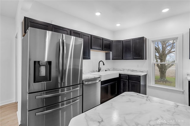 kitchen with sink, light stone countertops, stainless steel appliances, and light hardwood / wood-style flooring