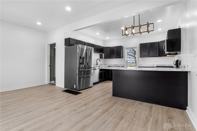 kitchen featuring kitchen peninsula, stainless steel appliances, a notable chandelier, light hardwood / wood-style floors, and hanging light fixtures