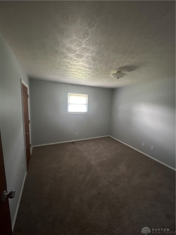 spare room featuring dark colored carpet and a textured ceiling