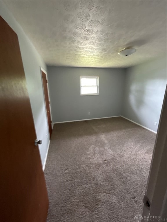 spare room with dark carpet and a textured ceiling