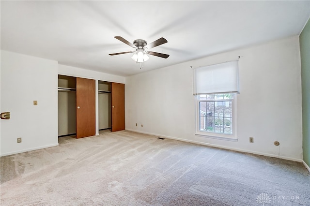 unfurnished bedroom featuring ceiling fan, light colored carpet, and two closets