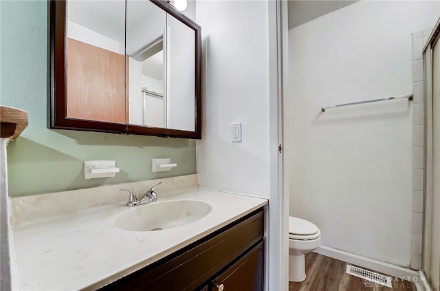 bathroom featuring toilet, vanity, a shower with shower door, and hardwood / wood-style flooring