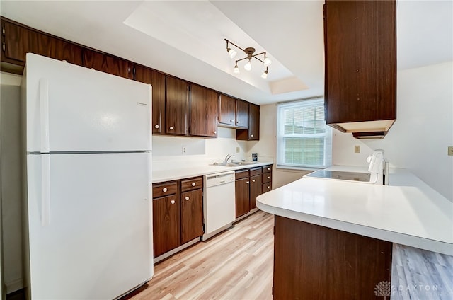 kitchen featuring white appliances, a raised ceiling, sink, light wood-type flooring, and kitchen peninsula