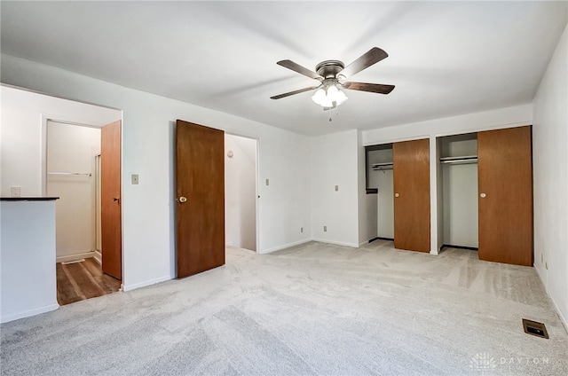 unfurnished bedroom with ceiling fan, ensuite bathroom, light colored carpet, and two closets