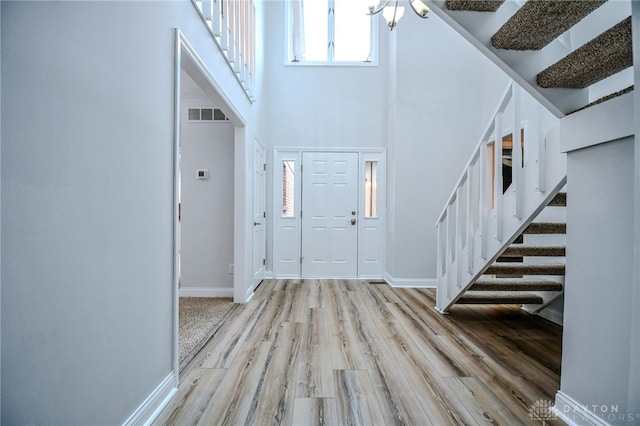 entrance foyer featuring a high ceiling, visible vents, baseboards, stairway, and light wood-type flooring