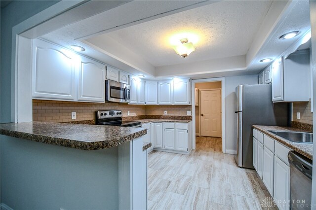 kitchen with stainless steel appliances, white cabinetry, a peninsula, and tasteful backsplash