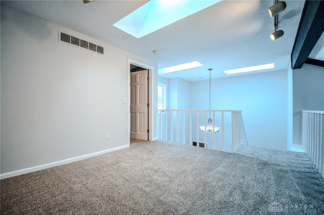 carpeted spare room featuring a chandelier, a skylight, visible vents, and baseboards