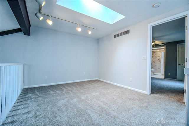 carpeted empty room with visible vents, baseboards, a ceiling fan, lofted ceiling with skylight, and rail lighting