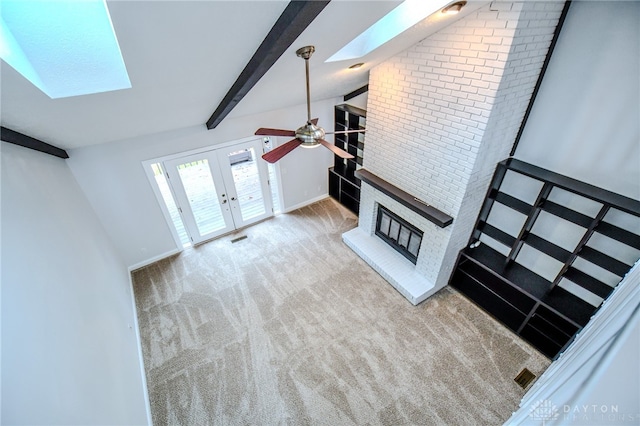 unfurnished living room with carpet floors, a fireplace, a ceiling fan, french doors, and lofted ceiling with skylight