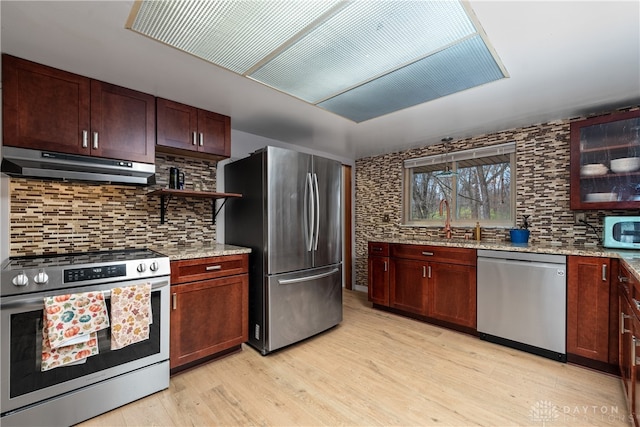 kitchen with decorative backsplash, light wood-type flooring, light stone counters, stainless steel appliances, and sink