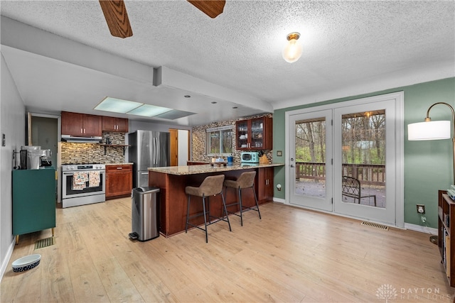 kitchen with ceiling fan, light wood-type flooring, a textured ceiling, appliances with stainless steel finishes, and kitchen peninsula