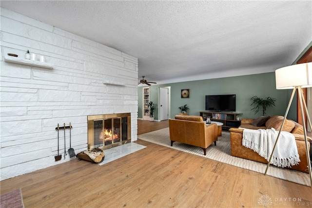 living room featuring a fireplace, hardwood / wood-style floors, a textured ceiling, and ceiling fan