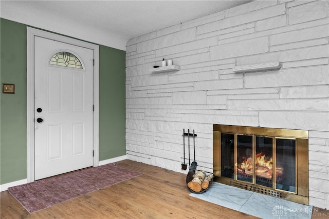 foyer entrance featuring a stone fireplace, hardwood / wood-style floors, and a textured ceiling