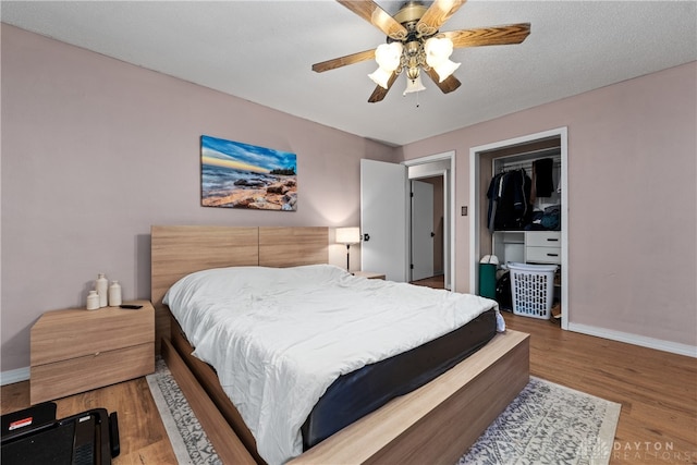 bedroom with hardwood / wood-style floors, a walk in closet, ceiling fan, a textured ceiling, and a closet