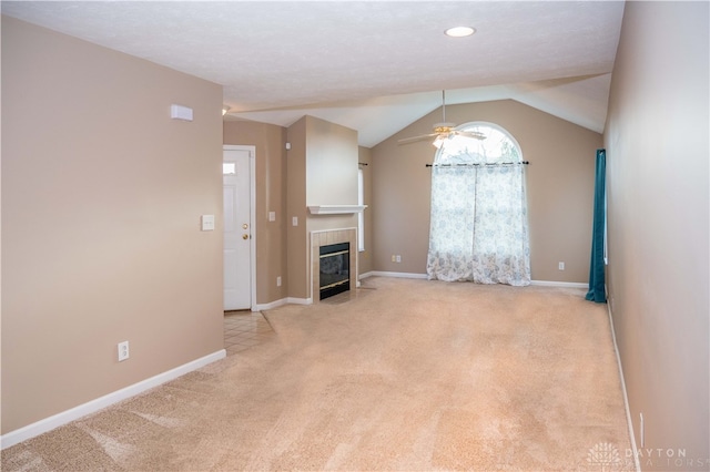 unfurnished living room with light colored carpet, ceiling fan, lofted ceiling, and a tiled fireplace